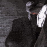 a man in a suit and tie is holding a bloody knife in front of a brick wall .