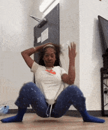 a woman in a white shirt and blue pants is squatting on the floor with her legs crossed .
