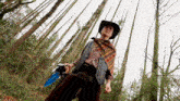 a man in a cowboy outfit is standing in a forest holding a blue sword