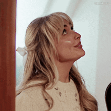 a woman wearing a white sweater and a white bow in her hair looks up .