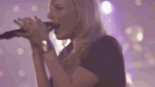 a woman is singing into a microphone with purple lights behind her