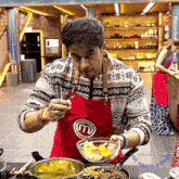 a man in a red apron with the letter m on it prepares food