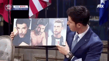 a man in a suit and tie is holding a painting of three men