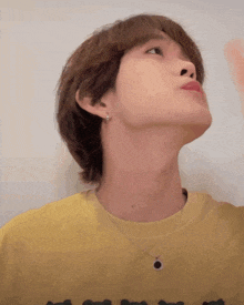 a man wearing a yellow shirt and a black necklace looks up