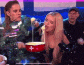 a woman is eating fondue from a red pot with a swiss cross on it