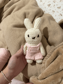 a person is holding a crocheted bunny with overalls on