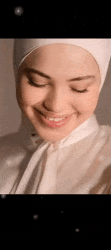 a close up of a woman wearing a hijab and a white shirt smiling .