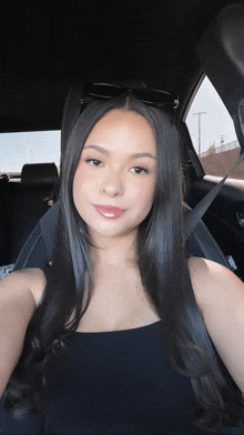 a woman sitting in a car wearing sunglasses and a black top
