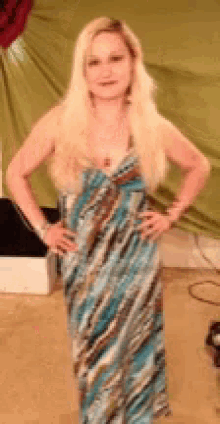 a woman in a long blue and brown dress stands with her hands on her hips