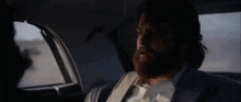 a man with a beard is sitting in the back seat of a car and talking to another man .