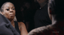 a woman in a black dress is talking to another woman in a dark room with the word zeus on the bottom