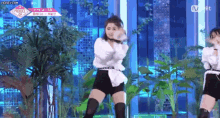 a woman in a white shirt and black shorts is dancing on a stage with plants in the background .