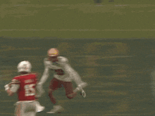 a football player in a red jersey and white pants is being tackled by another player on the field .