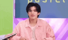 a young man in a pink striped shirt is holding a tablet in his hand .