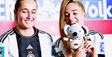 two female soccer players holding a stuffed koala in front of a sign that says " volks "