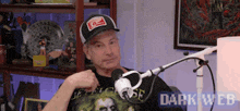 a man is sitting in front of a microphone wearing a hat and a black shirt .