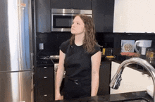 a woman in a black shirt stands in a kitchen