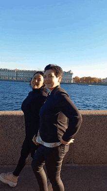 two women standing next to each other in front of a large body of water
