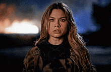 a woman with long blonde hair is standing in front of a burning building