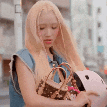 a woman with blonde hair is holding a purse and a helmet