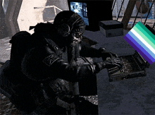 a man in a mask is typing on a laptop next to a green and purple flag