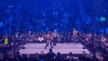 two wrestlers are standing next to each other in a ring while a referee looks on .