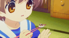 a little girl is eating sushi with chopsticks while wearing a blue and white uniform