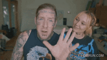 a man with a tattoo on his face and a woman behind him with a gifrun.com watermark