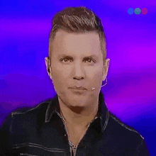 a man wearing a black shirt and a microphone looks at the camera on a purple background .