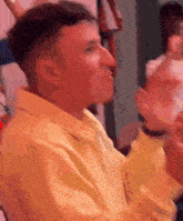 a man in a yellow shirt is making a funny face while sitting in a room .