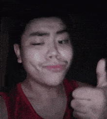 a man in a red tank top is giving a thumbs up sign .