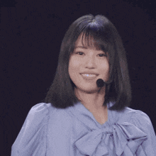 a woman wearing a blue shirt and a microphone on her head is smiling .