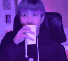 a man with purple hair is sitting in a chair drinking from a paper cup .