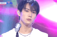 a young man stands in front of a microphone with the word show behind him