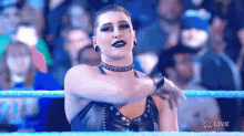 a woman in a black dress is standing in a wrestling ring with her arms outstretched .