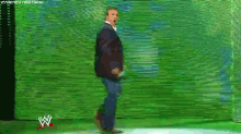 a man in a suit is walking in front of a green wall with a w on it