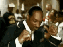 a man in a suit and tie is smoking a cigarette in a crowd .