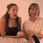 two women are sitting on a couch with a rode microphone between them
