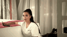 a woman in a white shirt is sitting on a couch holding a cell phone