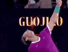 a man in a purple shirt is holding a tennis racquet in front of a sign that says guojiao