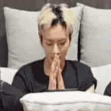 a man is sitting on a bed with his hands folded in prayer while looking at a tablet .