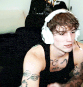a man wearing headphones and a black tank top has a tattoo on his chest that says ' u '