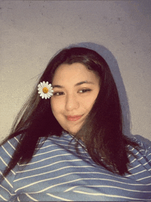 a girl wearing a blue and white striped shirt has a white flower in her hair