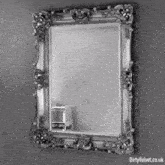 a black and white photo of a mirror with a gold frame hanging on a wall .