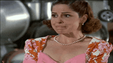 a woman wearing a pearl necklace and a pink top makes a funny face