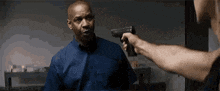a man in a blue shirt is pointing a gun at another man in a room .