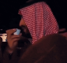 a man wearing a red and white checkered head scarf holds a cell phone