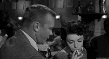 a black and white photo of a man and a woman smoking cigarettes in a bar .
