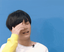 a young man is covering his face with his hand while wearing a yellow sweater