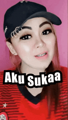 a woman wearing a baseball cap and a red shirt with aku sukaa written on it